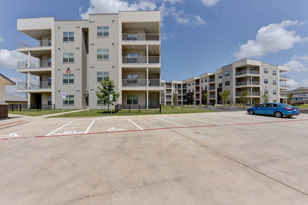 A parking lot in front of apartment buildings with a blue car parked.