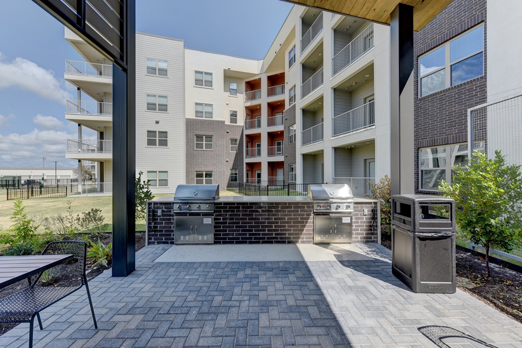 A modern apartment complex with a brick patio and recycling bins.