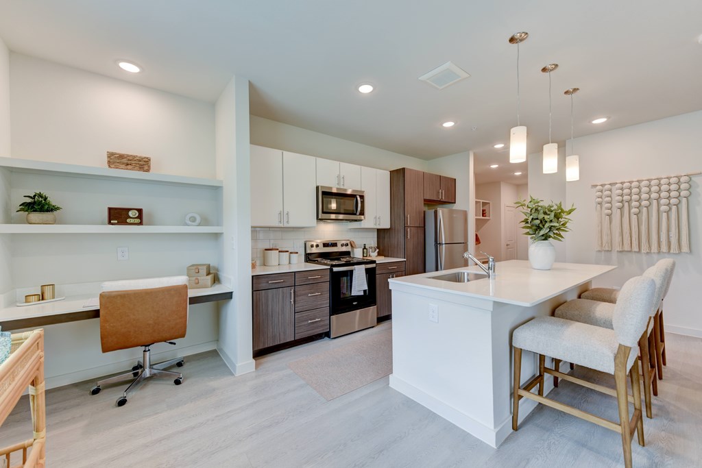 A modern kitchen with a white island and wooden chairs.