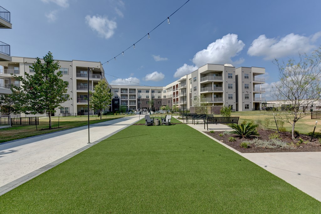 A grassy area in front of apartment buildings with a bench and trees.