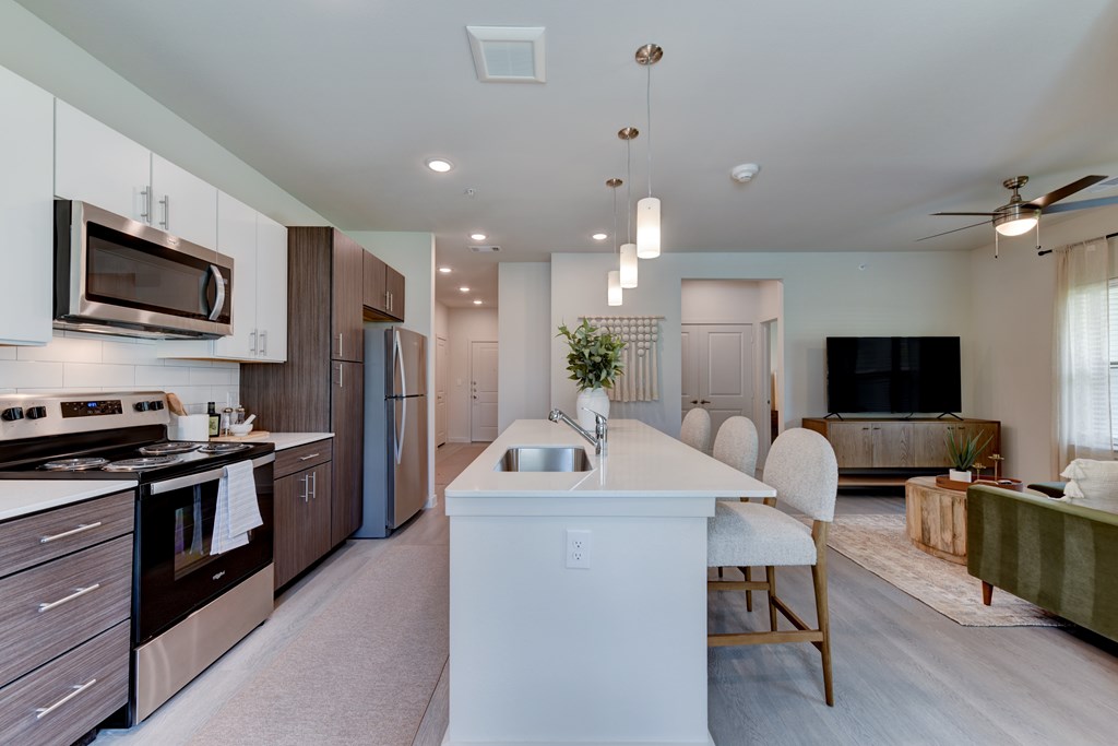 A modern kitchen with a white island and a TV in the living room.