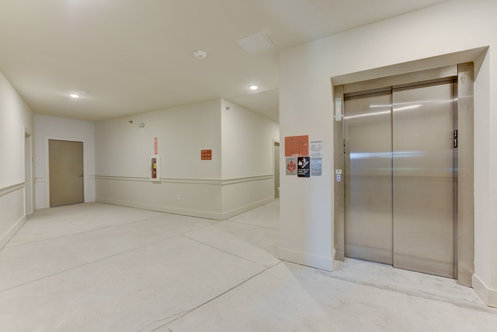 A white hallway with a glass elevator on the right.