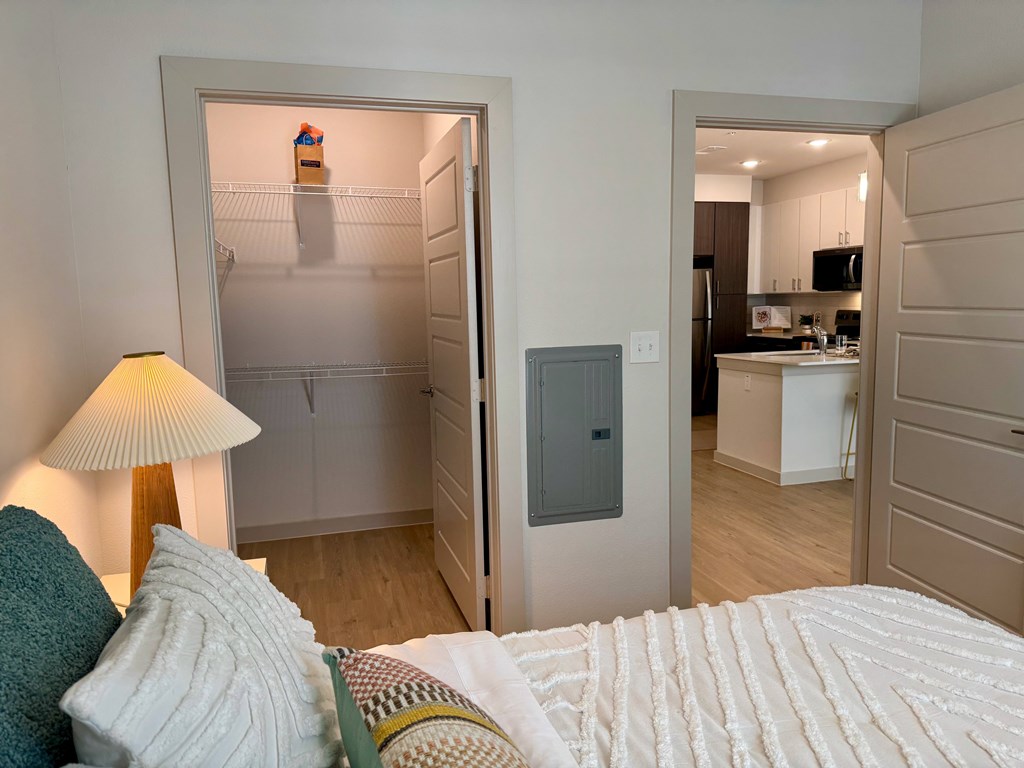 A bedroom with a bed, lamp, and a view into a kitchen.