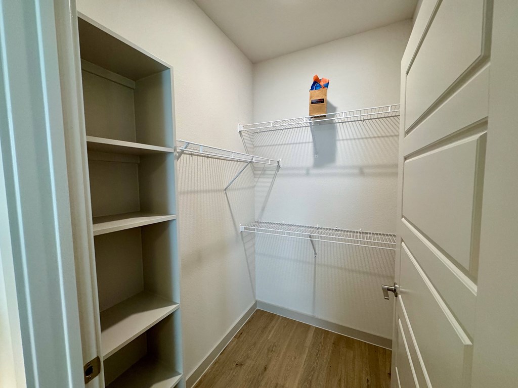 A small, empty walk-in closet with a shelf and a wire shelving unit.