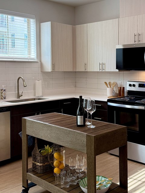 A kitchen with a wooden cart holding a bottle of wine and glasses.