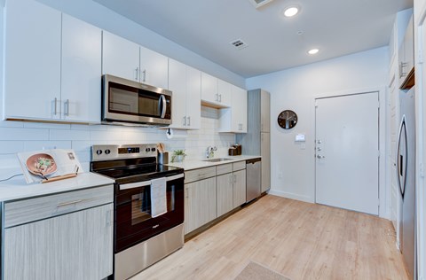 A modern kitchen with white cabinets and a wooden floor.