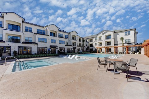 A large outdoor swimming pool surrounded by chairs and buildings at Bridge at Speyside Apartments, Texas