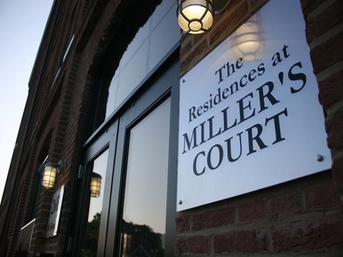 A sign that says "The Residences at Miller Court" is mounted on a brick wall.