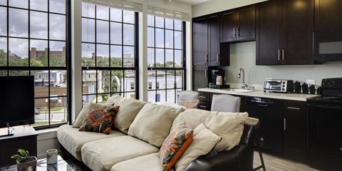 A living room with a couch and a kitchen area in the background.