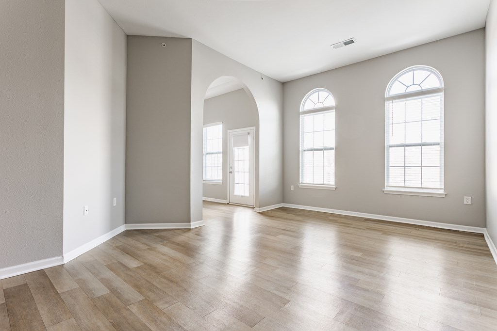 A room with wooden flooring and two windows.