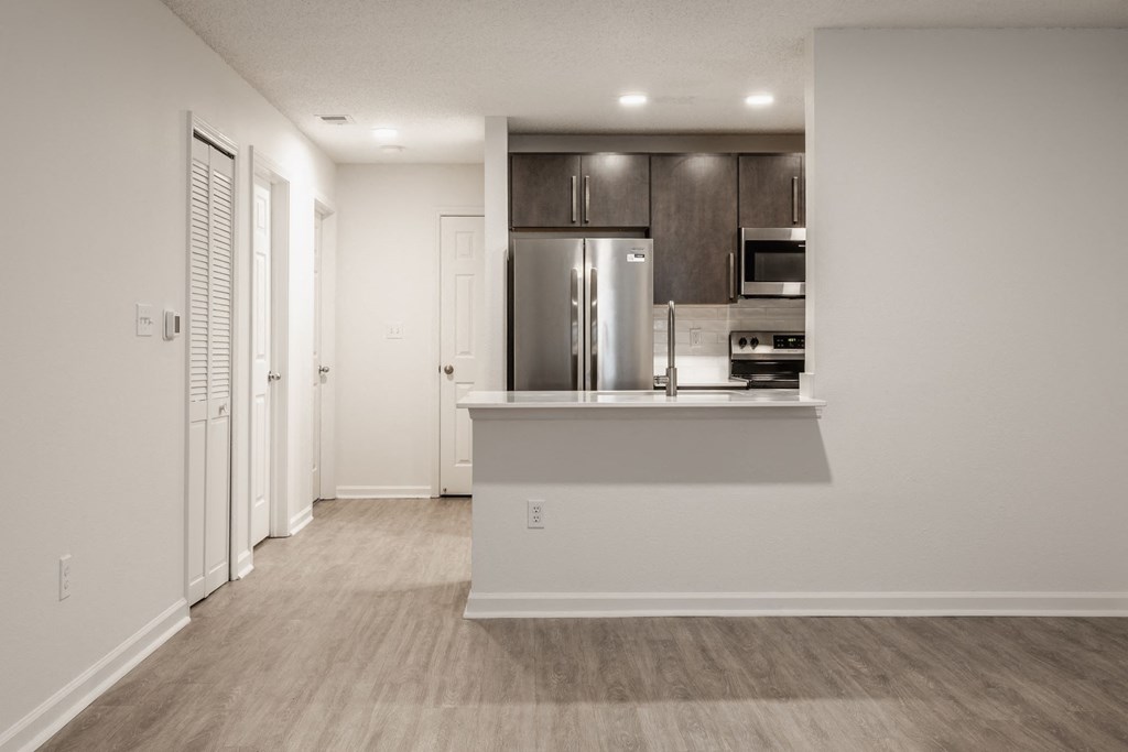 a living room with a kitchen and a door to a hallway at Latitudes Apartments, Indianapolis, IN