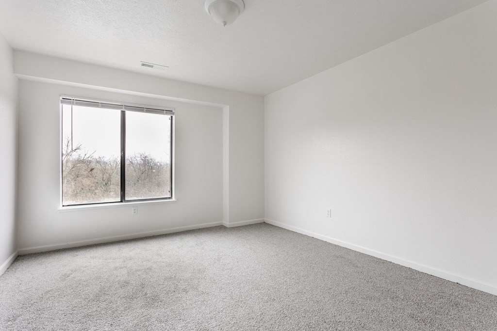A room with a carpeted floor and a window showing a tree outside at Huntington Cove Apartments, Merrillville, IN, 46410