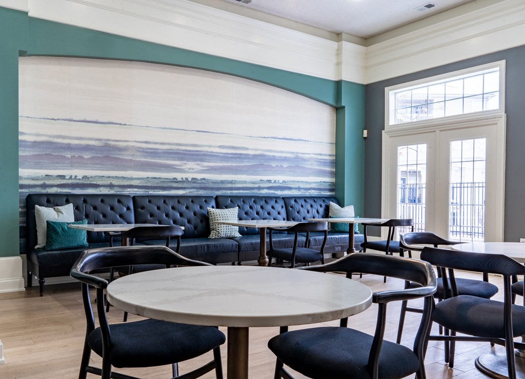 a seating area with tables and chairs and a large painting on the wall at Latitudes Apartments, Indianapolis, IN