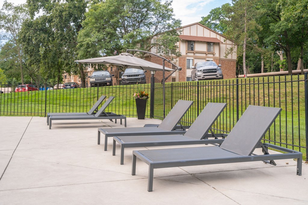 a row of chaise lounges in front of a fence with a house in the at Cordoba Apartments, Michigan, 48334