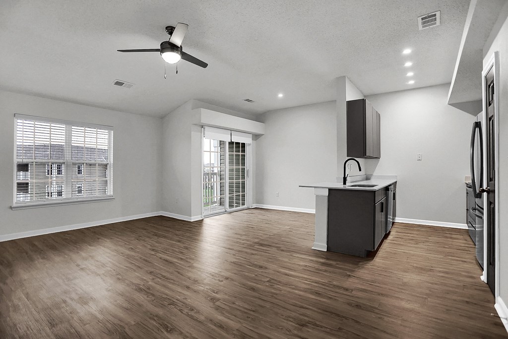 an empty living room with a kitchen and a ceiling fan at Latitudes Apartments, Indianapolis, IN