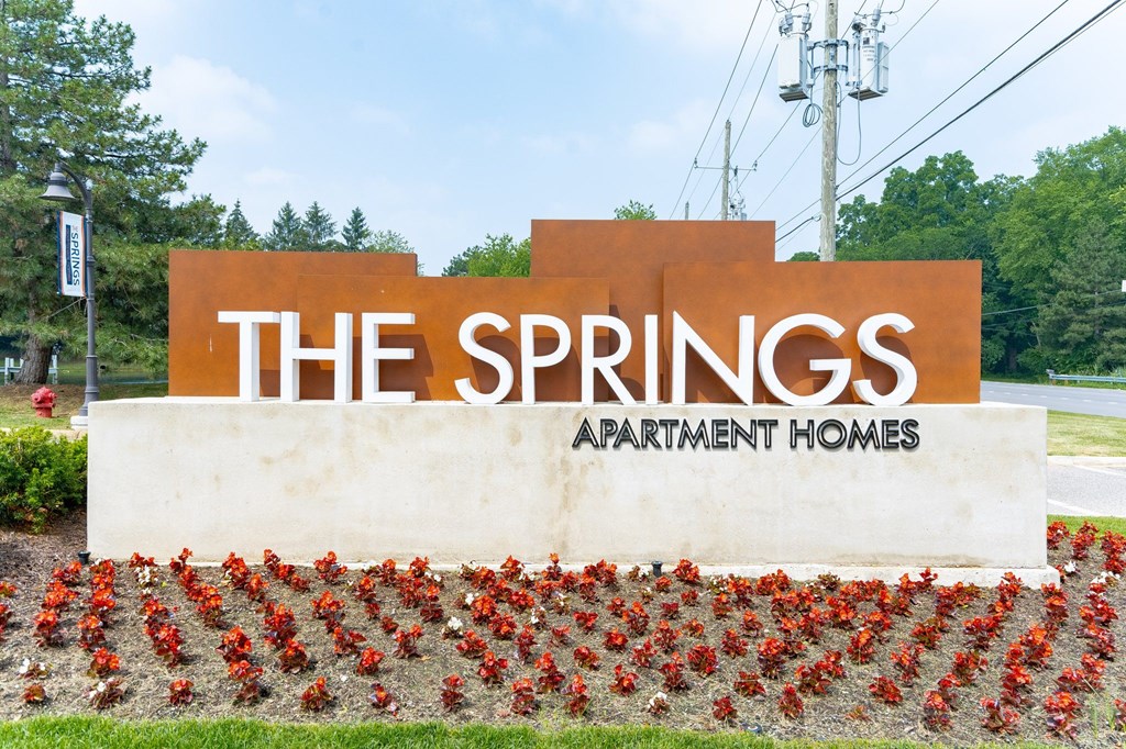 a sign for the springs apartment homes with red flowers in front of it at The Springs Apartment Homes, Michigan