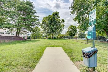 a walkway to a dog park with a blue trash can on it
