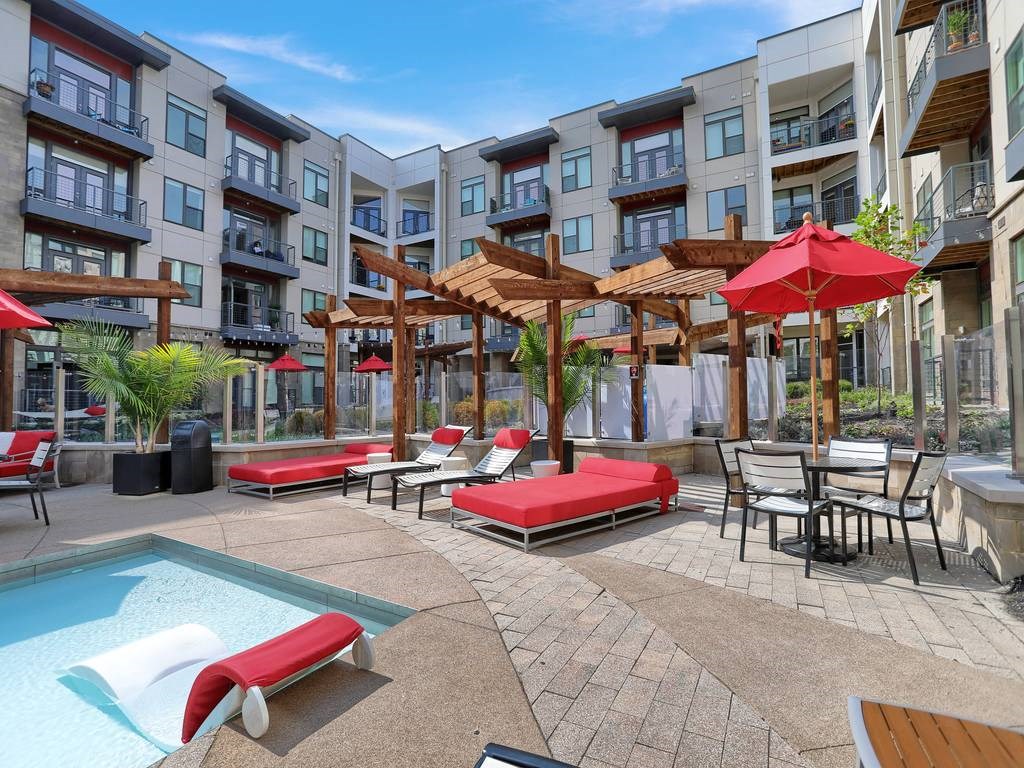 a pool with lounge chairs and umbrellas in front of an apartment building  at Avant & Avant II, Carmel, IN, 46032