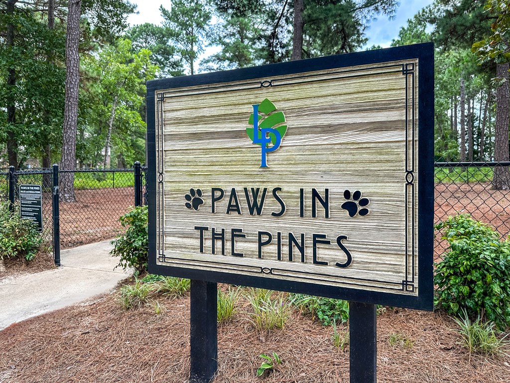 A wooden sign that says "Paws in the Pines" is in front of a fence.