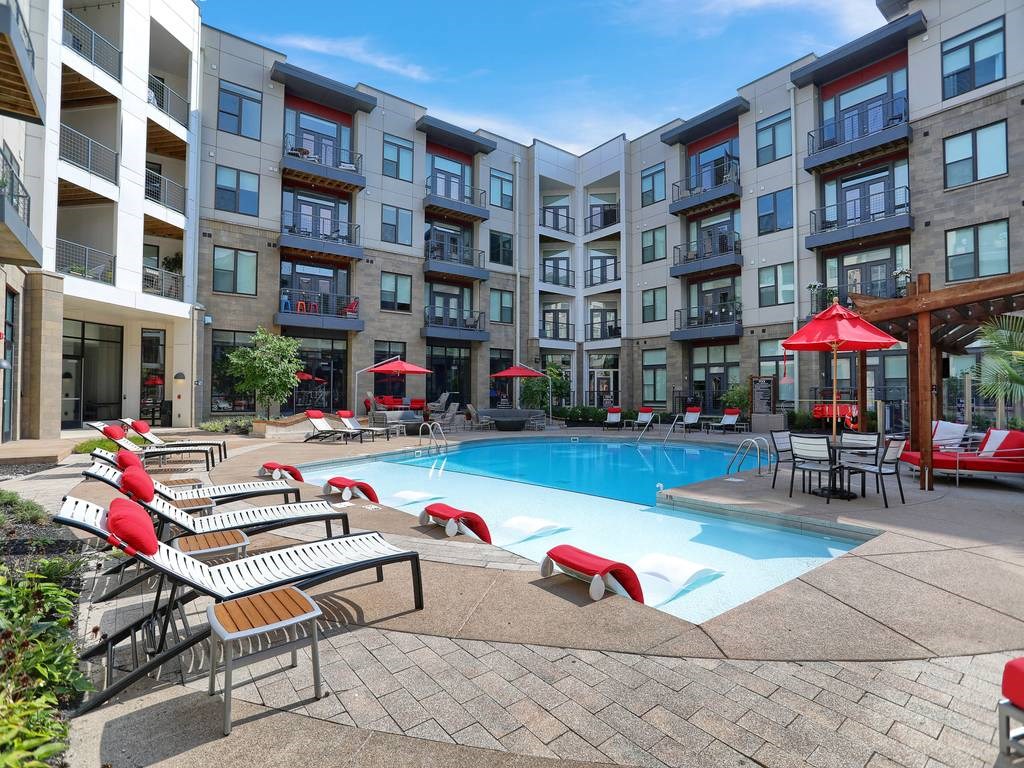 a swimming pool with chaise lounge chairs and umbrellas in front of an apartment building  at Avant & Avant II, Carmel, IN