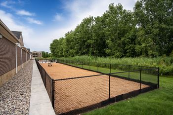 A tennis court is surrounded by a black fence and a gravel path.