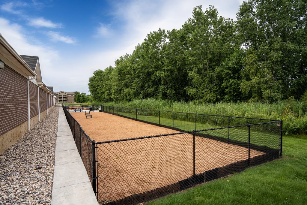 A tennis court is surrounded by a black fence and a gravel path.