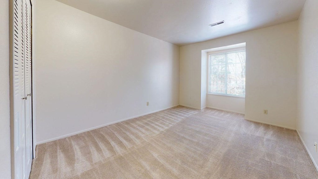 an empty bedroom with a large window and plush carpet at Apple Ridge Apartments, Michigan, 49534