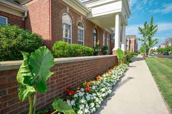A brick building with a white porch and a flower bed in front.