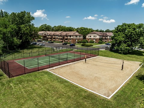 A tennis court surrounded by a fence and trees with apartment buildings in the background