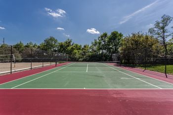 A tennis court with a red surface and green boundary lines at Autumn Woods Apartments, Miamisburg