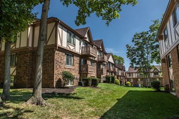A tree stands in front of a building with a lawn in front of it. at Autumn Woods Apartments, Miamisburg, OH, 45342