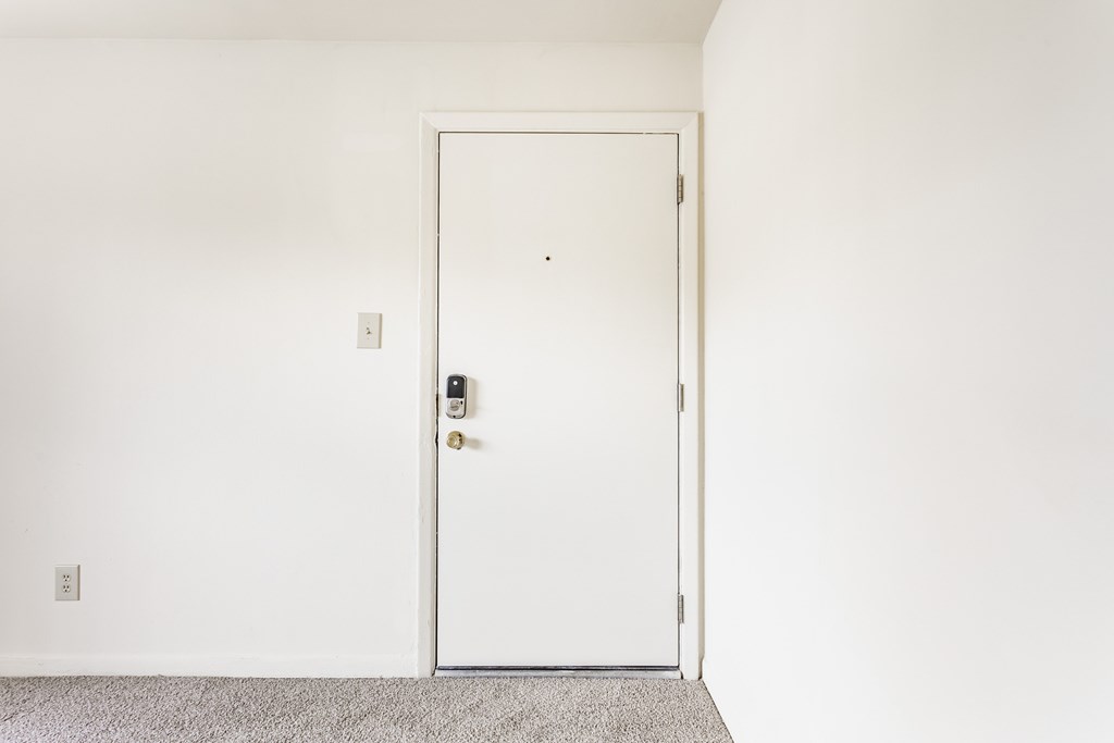 A white door with a handle and a keypad is in a room with a grey carpet