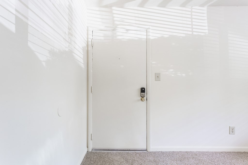 A white door with a black handle and lock in a white room