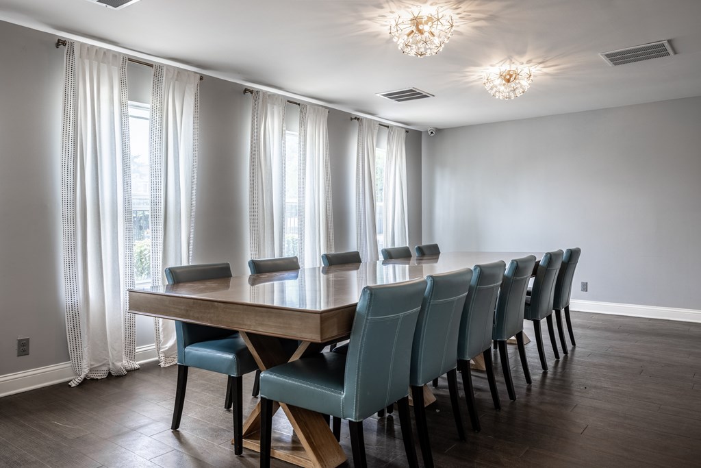 A long wooden table with blue chairs is in the middle of a room with a window