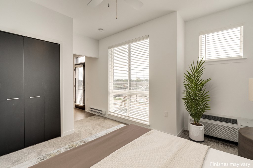 a bedroom with a large window and a large potted plant  at Uptown Square Apartments, Michigan, 48083