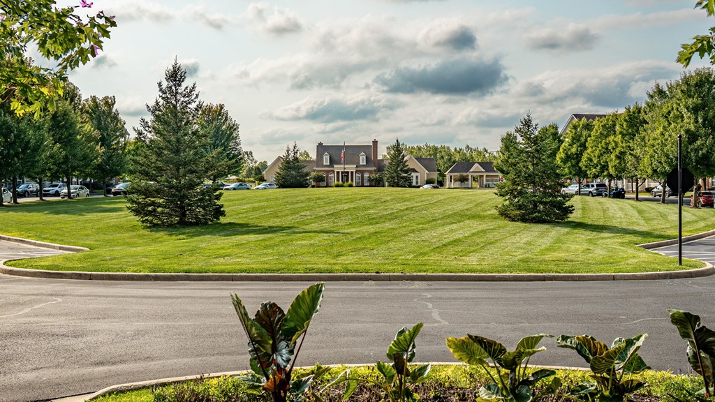 A large building is surrounded by a green lawn and trees