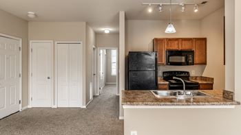 A kitchen with a black fridge and microwave, and a hallway with white doors