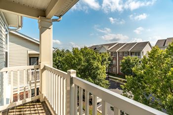 A balcony with a white railing overlooks a street with houses and trees