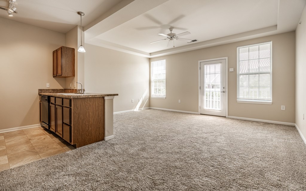 A spacious living room with a carpeted floor and a ceiling fan