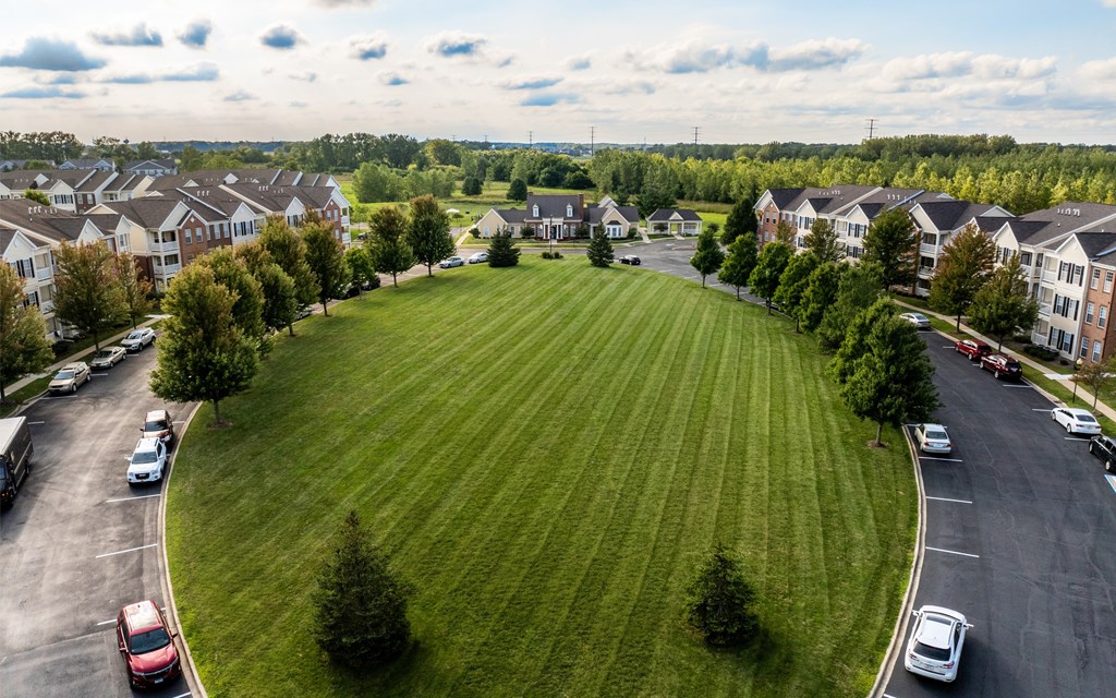 A large grassy area surrounded by apartment buildings and cars parked in a lot