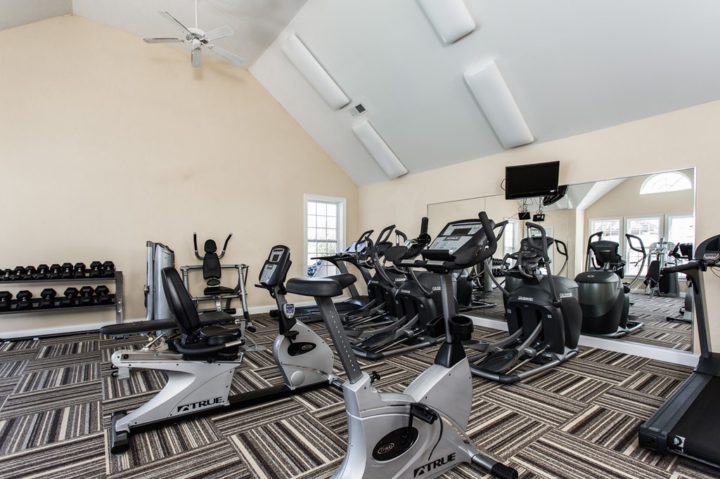 A gym with a variety of exercise equipment including treadmills, stationary bikes, and weight machines