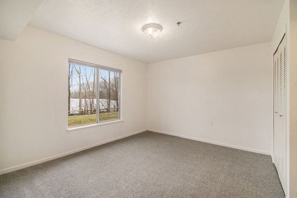 Bedroom with a large window and carpet at Canal 2 Apartments, Lansing, Michigan