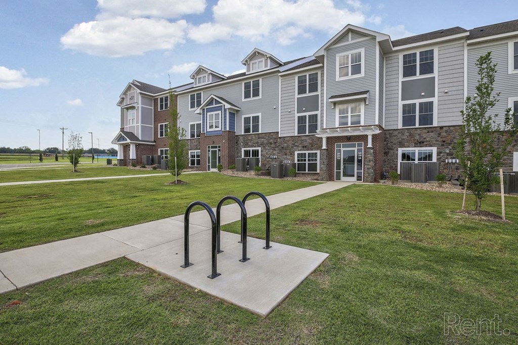 an apartment building with a bike rack on the sidewalk at Dodson Pointe Apartment Homes, Rogers