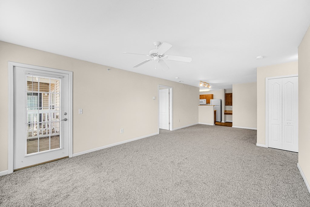 an empty living room with a door to a kitchen and a ceiling fan at Brickshire Apartments in Merrillville, IN 46410