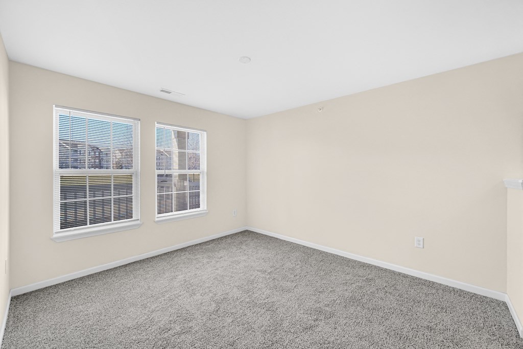 an empty bedroom with two windows and carpeting at Brickshire Apartments in Merrillville, IN 46410