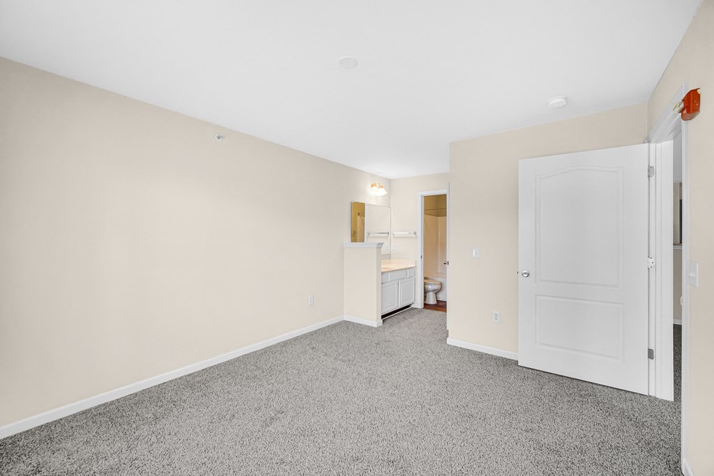 a bedroom with white walls and carpet and a door to a bathroom at Brickshire Apartments in Merrillville, IN 46410