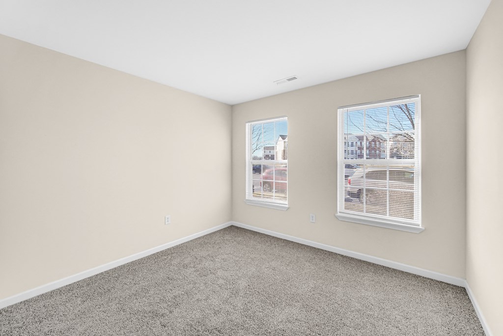 an empty room with carpet and two windows at Brickshire Apartments in Merrillville, IN 46410