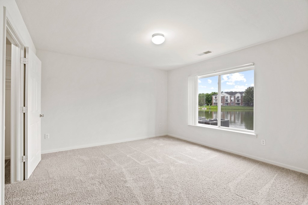 A room with a carpeted floor and a window showing a view of a house and trees.