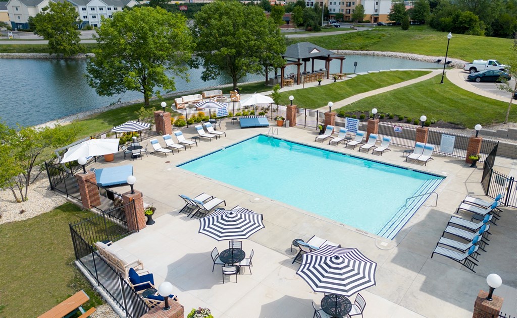 a swimming pool with chaise lounge chairs and umbrellas next to a body of waterat Sundance at The Crossings Apartments, Indy
