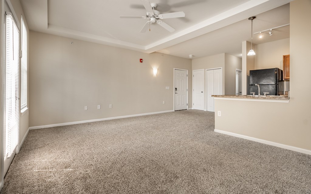 A spacious living room with a ceiling fan and carpeted floor